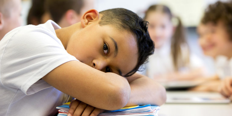 A close up shot of a little boy at school who looks distant and upset.